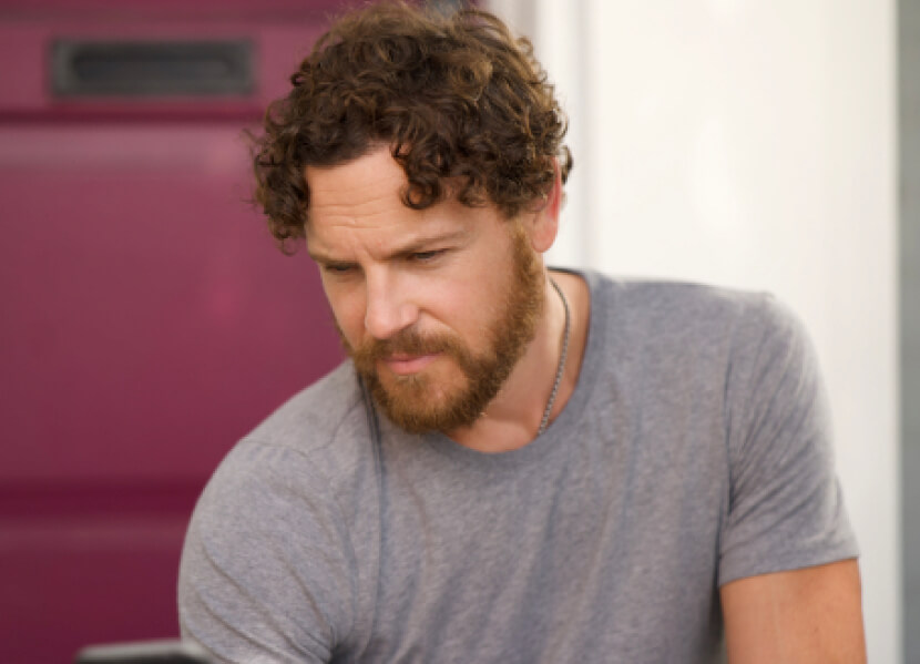 An image of an actor wearing a grey shirt looking confident after his hair transplant surgery by Dr. Jae Pak